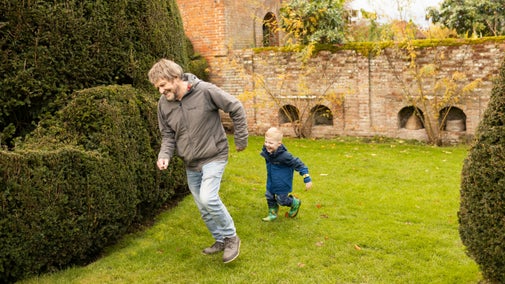 A father and young son chasing each other in the Yew Garden in November at Packwood House, Warwickshire